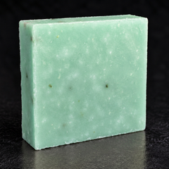 Sea-green Fresh Obsession soap bar with exfoliant flecks on a dark studio surface.
